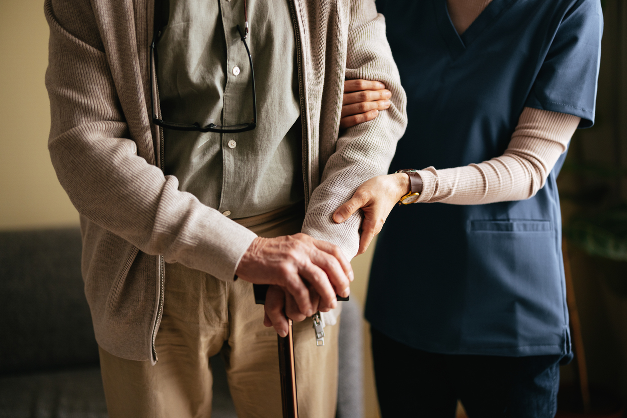 Caregiver assisting elderly person with a cane.