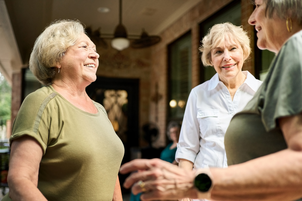 Group of older women smiling and talking outside.