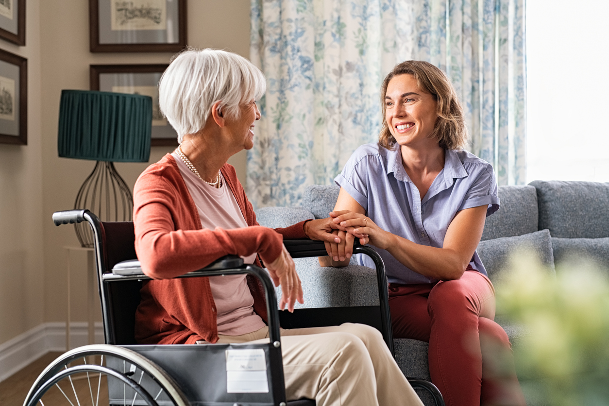 Caregiver smiling with elderly woman in wheelchair.