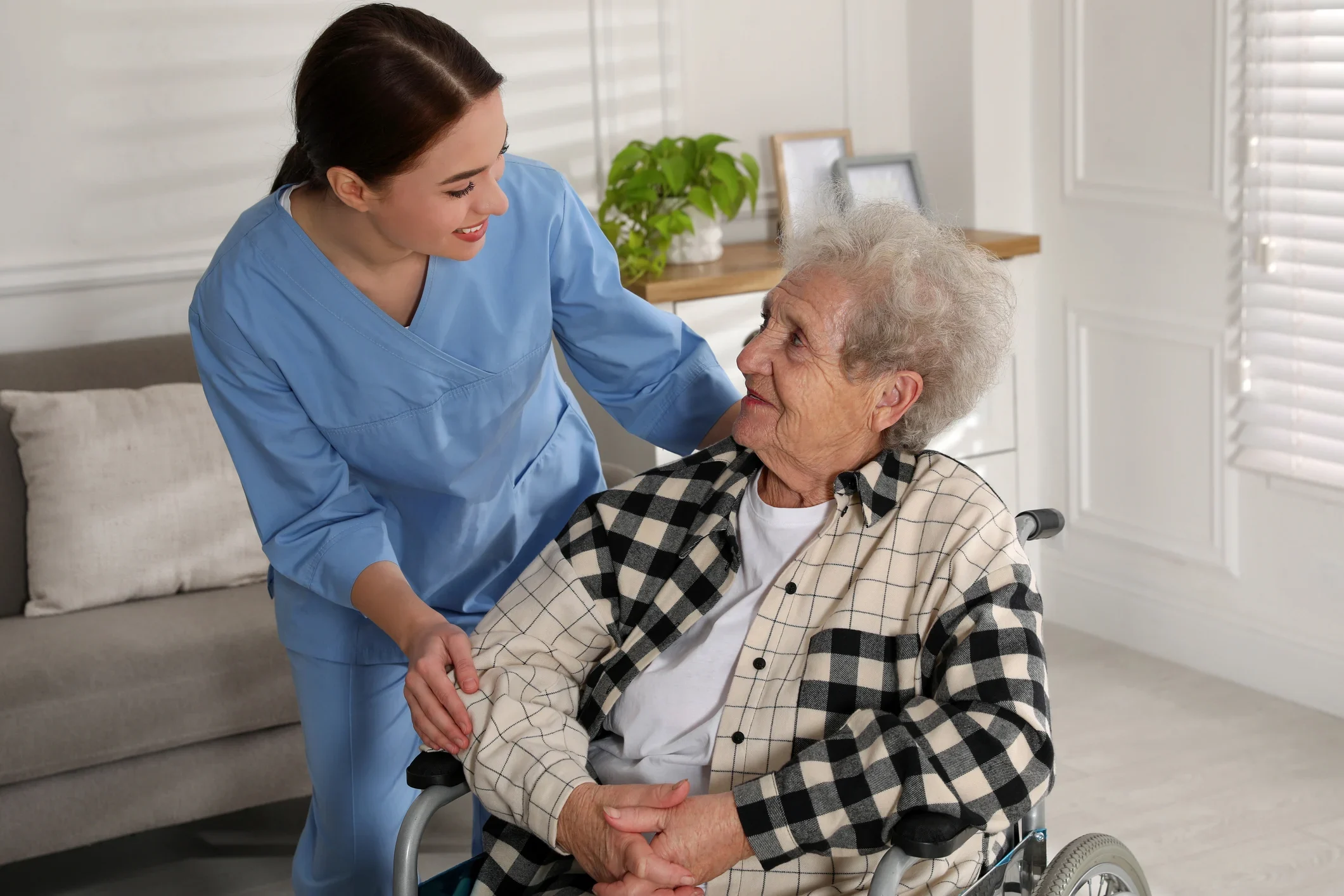 Caregiver assisting elderly person in wheelchair at home.