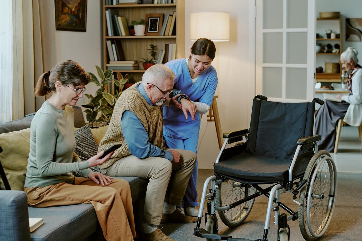 Nurse assisting elderly man with wheelchair indoors.