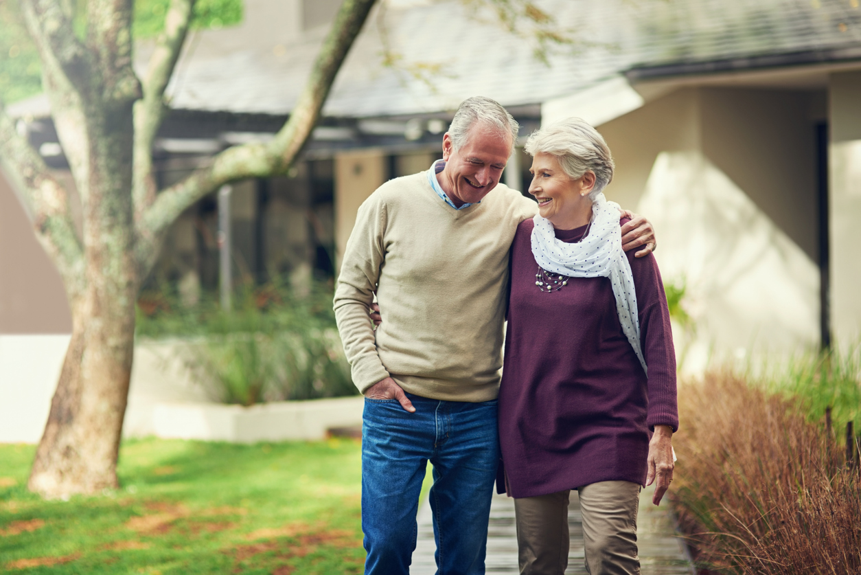 Smiling elderly couple walking arm in arm outdoors.